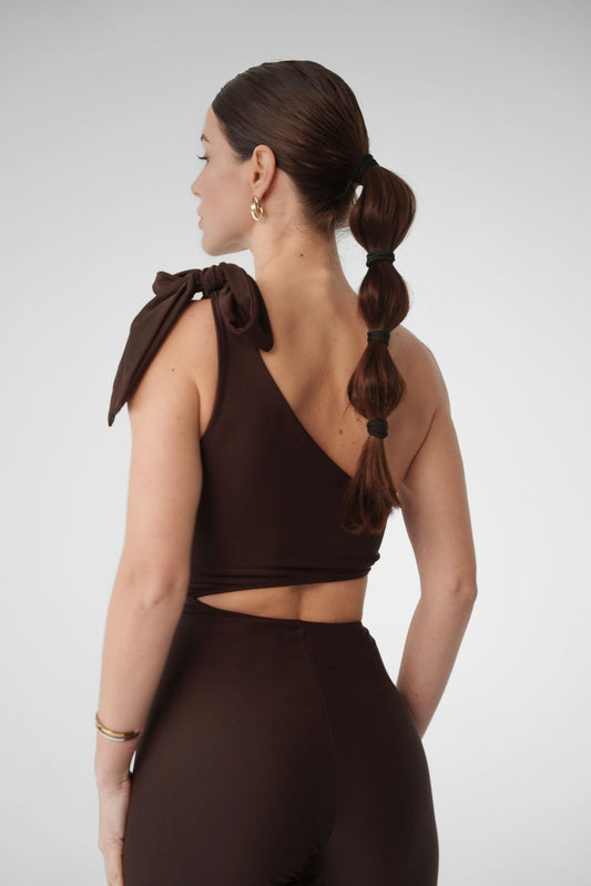 Model wearing Dominica brown one-shoulder jumpsuit with bow strap and leggings