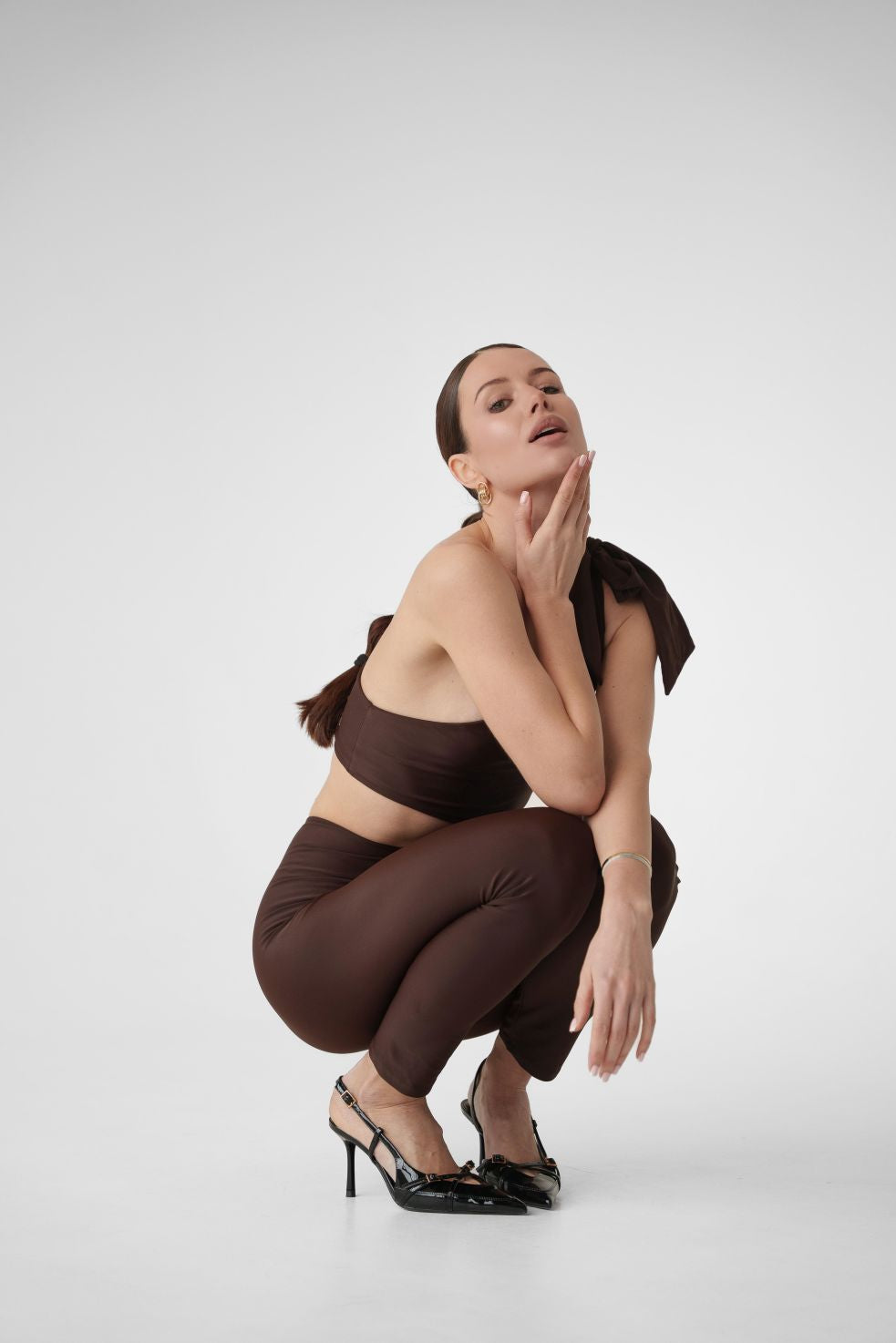 Model wearing Dominica brown one-shoulder jumpsuit with bow strap and leggings