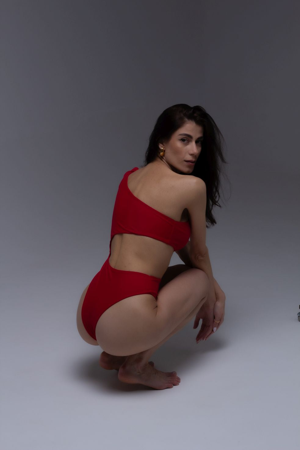 Model wearing Dominica red one-shoulder cut-out swimsuit with bow tie