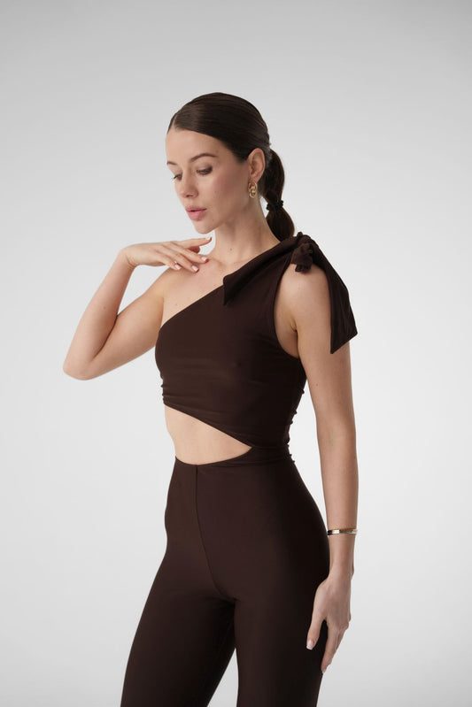 Model wearing Dominica brown one-shoulder jumpsuit with bow strap and leggings